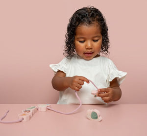 Lacing Beads, formine da infilare, Little Dutch. In foto bambina che infila lo spago nella formina del gioco a tema Fiori e Farfalle