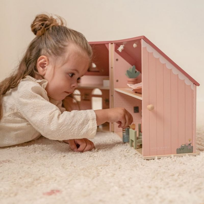 Bimba che gioca su un tappeto con la casa delle bambole aperta
