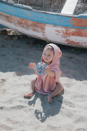 Massasggiagengive a pallina in silicone, Bamboom. In foto bambina seduta in spiaggia che gioca con il dentaruolo verde oceano