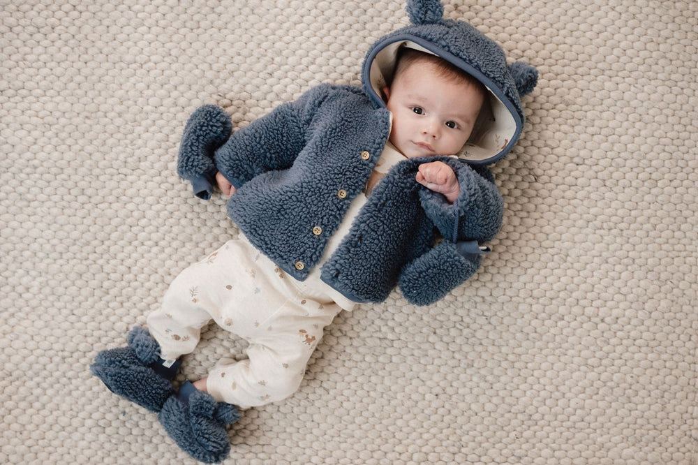 bimbo che indossa guanti e giacca e babbucce blu
