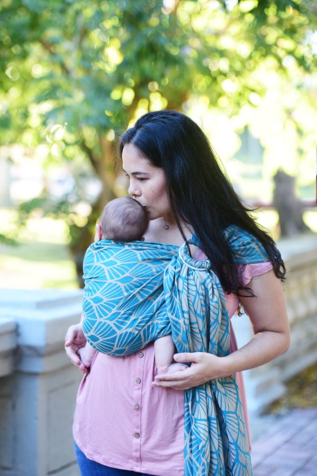 Fascia ad anelli Portabebè, Neko Slings, Modello KIDONYA MARINA. Fascia ad anelli azzurra con pattern a conchiglia. Madre che porta il bambino nella posizione davanti cuore a cuore