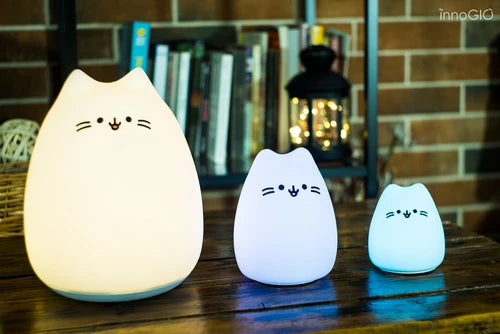 Luce a led notturna in silicone MINI, InnoGIO. Lampada a forma di gattino in silicone bianco con occhi, musetto e baffi neri. Vista della lampada a forma di gattino nelle tre dimensioni: grande, media e mini. Le tre lampade sono accese