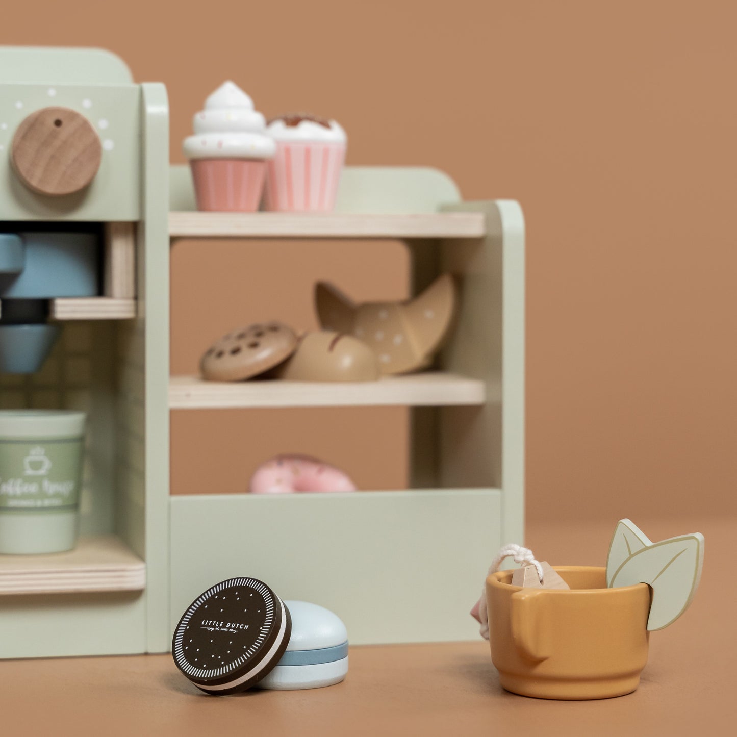 Coffee Corner, caffetteria in legno, Little Dutch. Particolare della tazza con all'interno bustina del te e foglie di menta e vicino due dolcetti. Caffetteria sullo sfondo