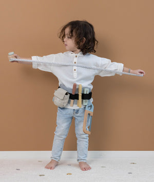 Cintura degli attrezzi in legno, Little Dutch. Cintura regolabile nera in tessuto con asole porta attrezzi e sacchetto per viti. Lima, taglierino, metro, pinze e sega. Bambino che gioca con il metro e indossa la cintura attorno alla vita.