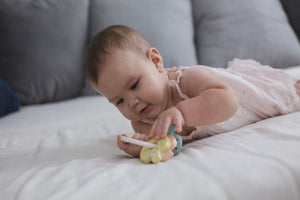 Sonaglio portachiavi in legno, Plan Toys. Bambina piccola che gioca sdraiata sul letto con il sanaglio.