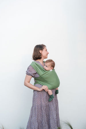 mamma in piedi di lato con bimbo legato in fascia verde
