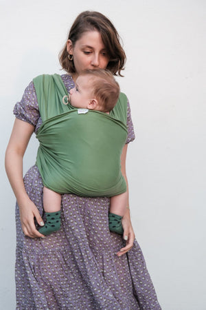 mamma che porta davanti bambino in fascia elastica verde