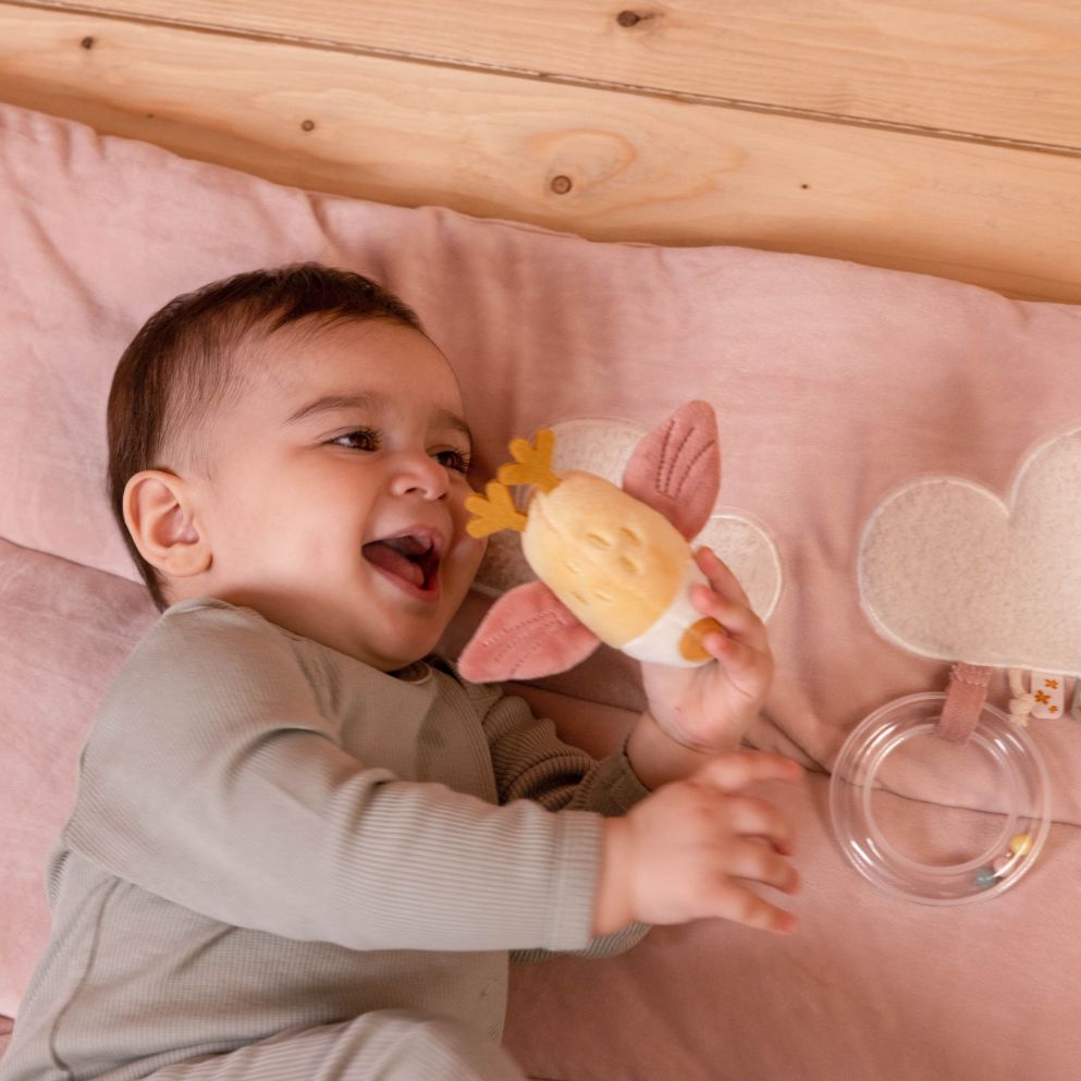 Tappeto morbido PlayPen Mat a tema Fiori e Farfalle, Little Dutch. Bambino coricato sul tappeto con in mano l'uccellino piccolo, giochino attaccato al tappeto